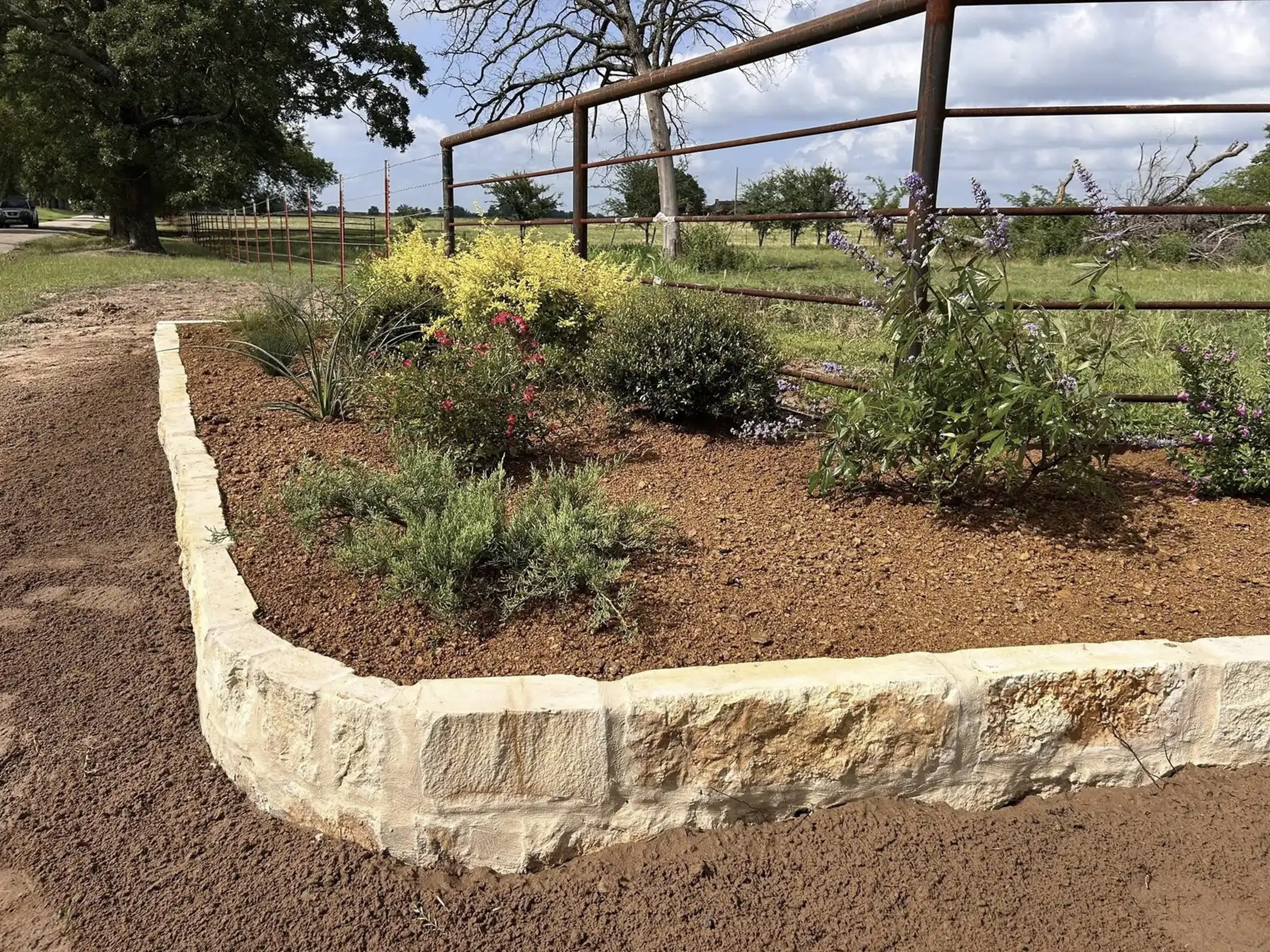 Decorative stone border with fresh landscaping, shrubs, and flowers along ranch-style fencing – Hood Lawn Care and Services