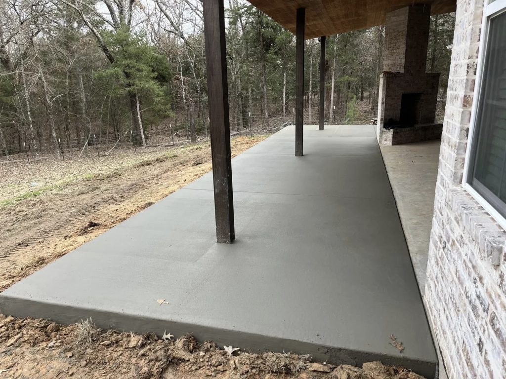 Newly poured concrete patio with smooth finish under covered porch, ideal for outdoor living – Hood Lawn Care and Services