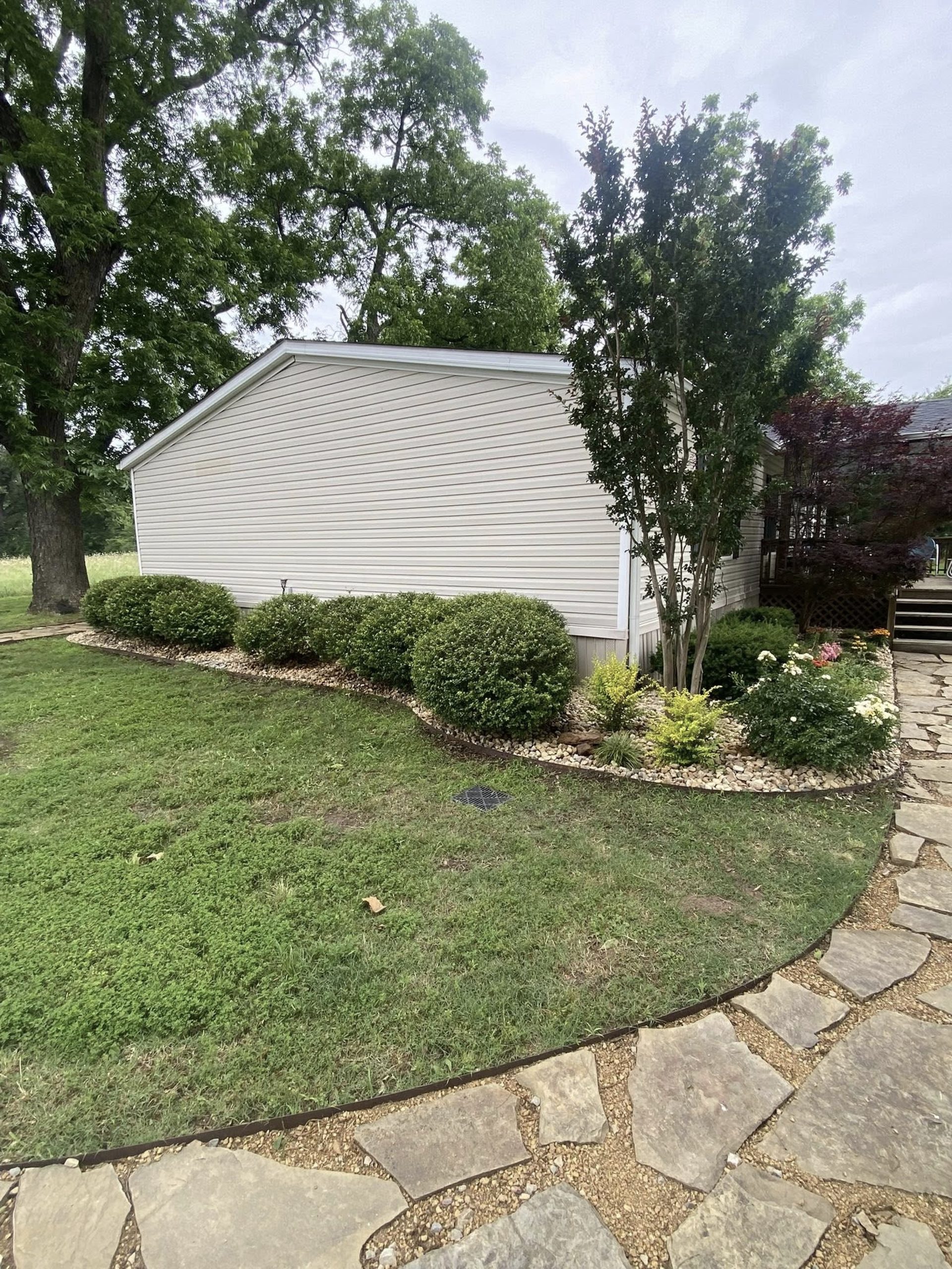 Residential landscape with stone walkway, trimmed shrubs, and decorative rock flower bed by Hood Lawn Care