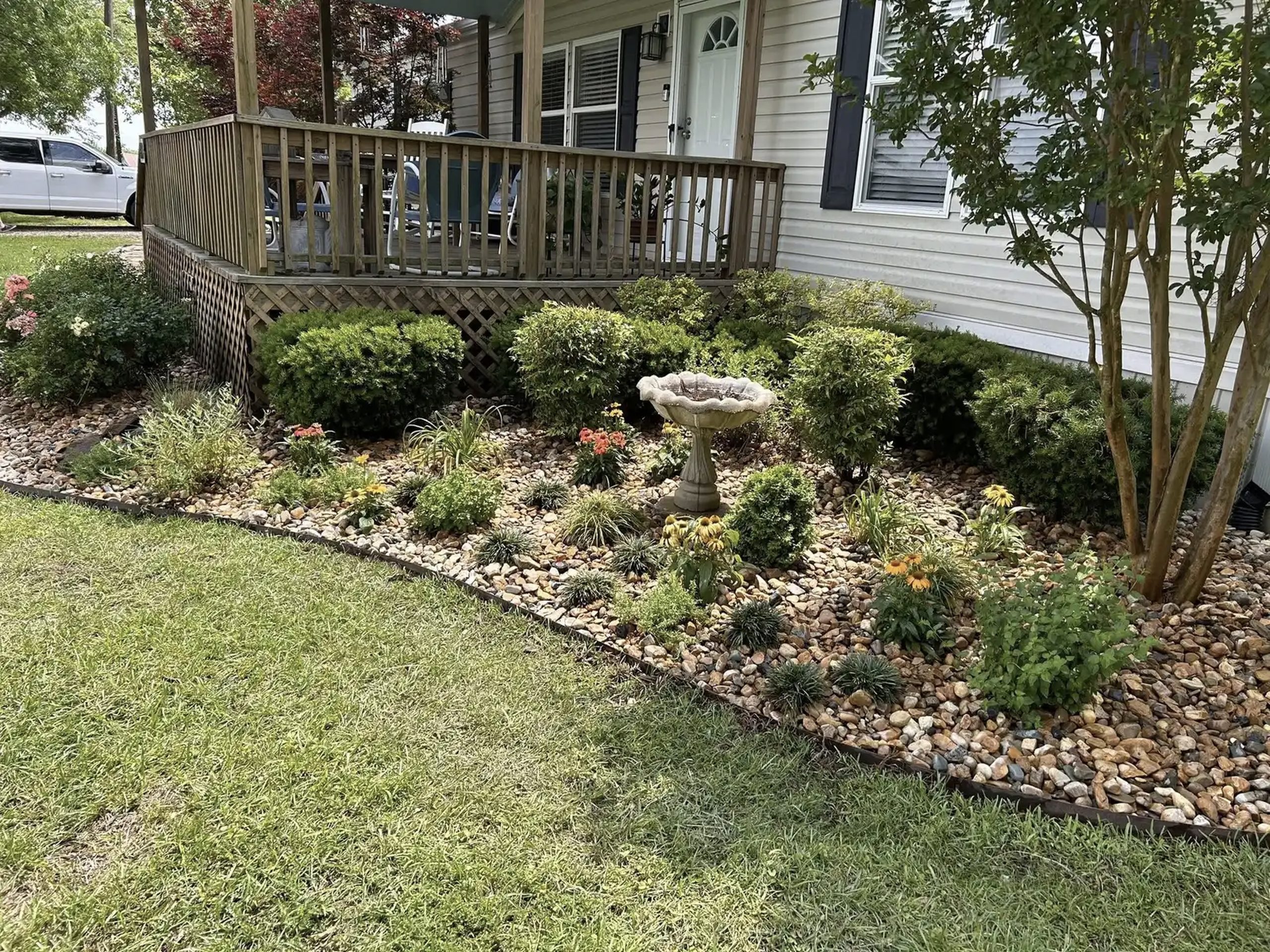Residential landscape design with rock garden, trimmed shrubs, bird bath, and flower bed installed by Hood Lawn Care.